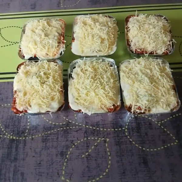 Six lasagnes individuelles maison en barquettes, couvertes de fromage râpé avant cuisson